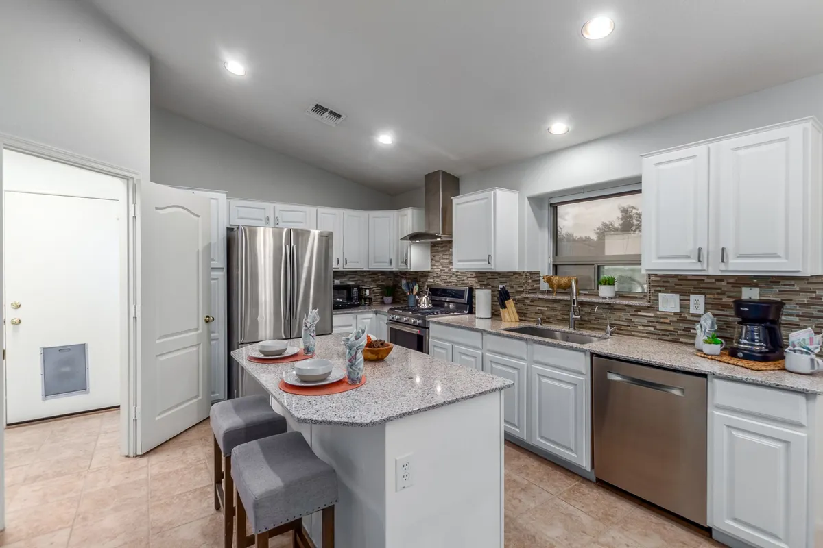 A bright, contemporary kitchen featuring a granite countertop, stainless steel appliances, and a breakfast bar with comfortable seating. The setup invites both casual morning coffees and lively group meal preps, with a modern touch that feels both welcoming and functional.
