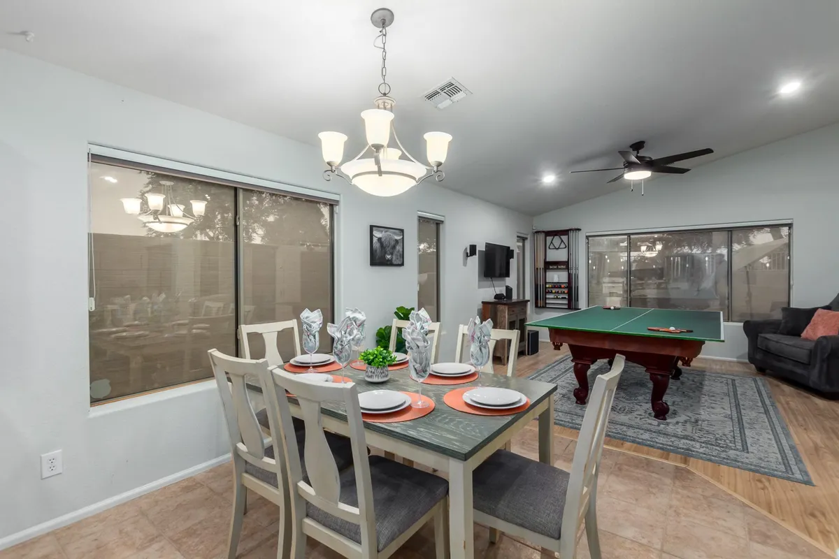 This lively interior shot showcases a multi-functional room with a dining table and a pool table beneath a chandelier. The space is designed for dining, playing games, and lively conversation, supporting a range of group activities and entertainment options.