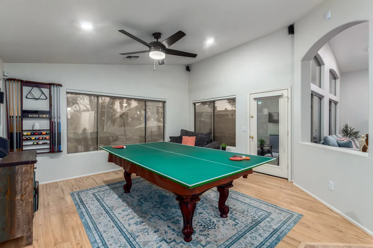 A lively game room bathed in natural light, featuring a pool table as the centerpiece, comfortable seating along the windows, and a spacious layout designed for games and relaxation.