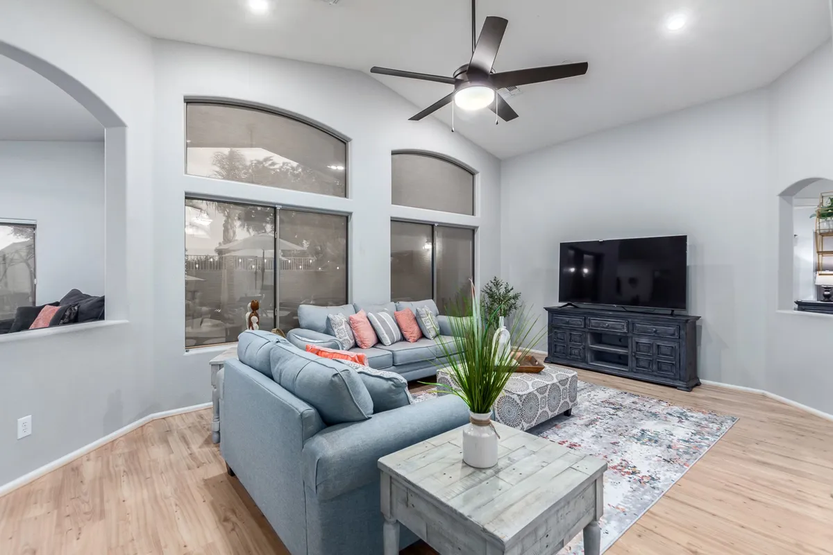 A cozy living area with a light blue sofa, colorful cushions, a large wall-mounted TV, a wooden coffee table, and a decorative rug. Sunlight pours in, creating a cheerful, relaxed ambiance ideal for families or groups.
