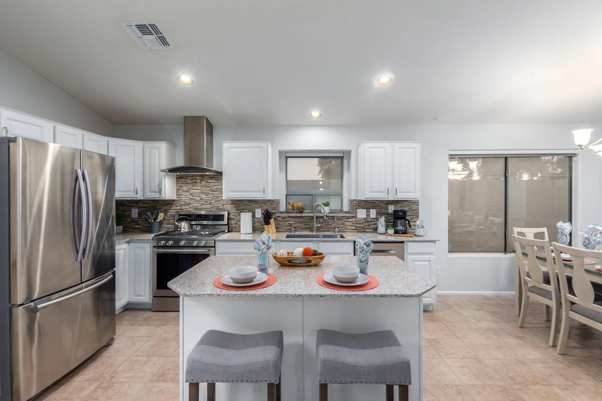 A modern kitchen showcasing a large island with bar seating, gleaming stainless steel appliances, and a dining area set for eight. The scene suggests a setting ready for both family meals and festive occasions, with soft, welcoming lighting highlighting the clean design.