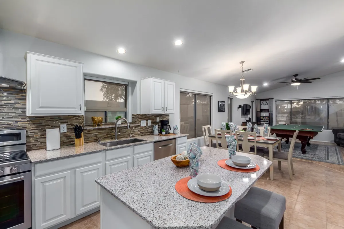 The image presents a spacious interior game room with a pool table, kitchen island, and dining area. The open layout is conducive to socializing, playing games, and enjoying shared meals.