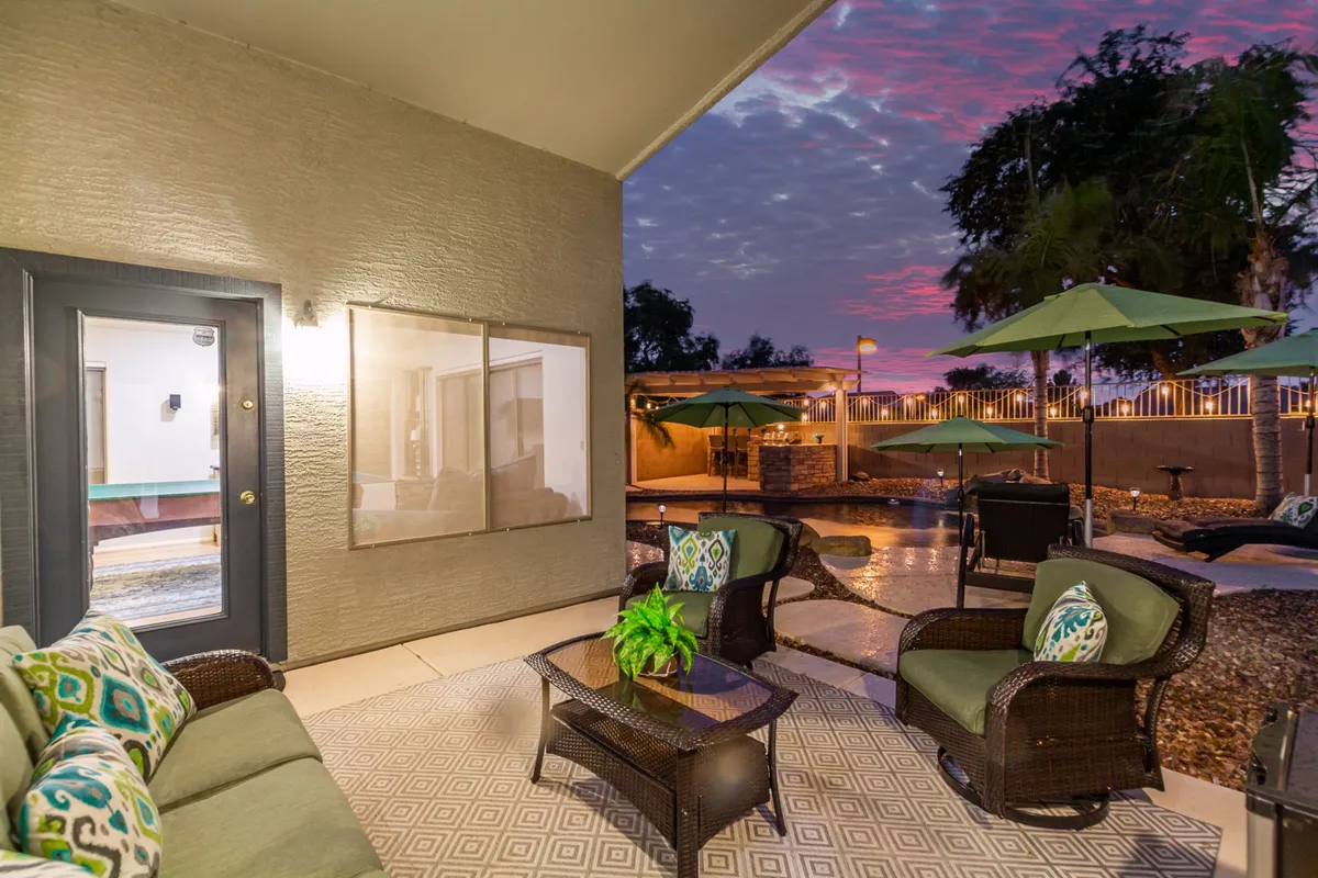 This exterior shot features a spacious outdoor seating area overlooking the swimming pool, with large umbrellas providing shade. The landscaping, evening lighting, and visible sunset sky create a serene environment for gatherings and relaxation.