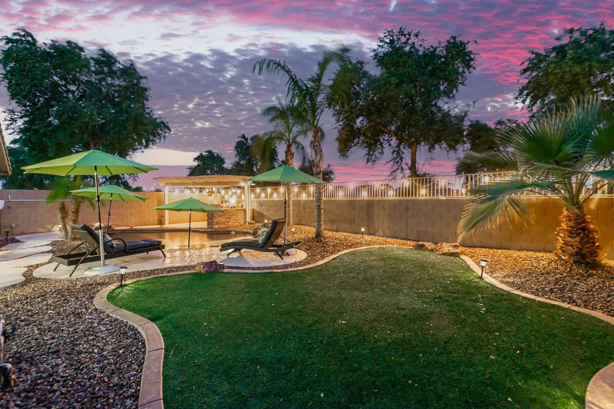 An inviting backyard patio with green umbrellas, lounge chairs, stone patio, and palm trees. The serene outdoor setup suggests a safe, fenced space for pets to play and for guests to relax while enjoying the outdoors together.