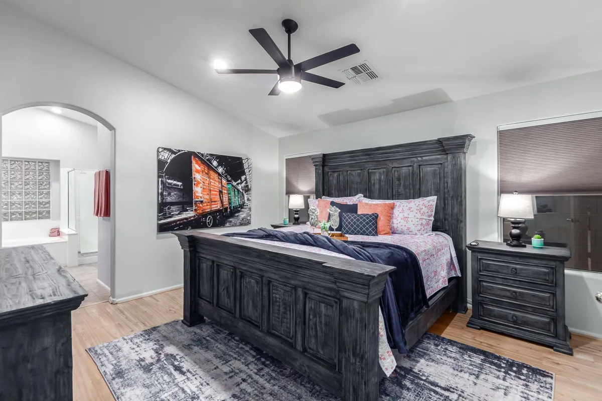 A comfortable bedroom featuring a dark wood bed frame with vibrant, colorful bedding, abstract wall art above the headboard, and nightstands with lamps on either side. The mood is both stylish and restful, ideal for cozy evenings.