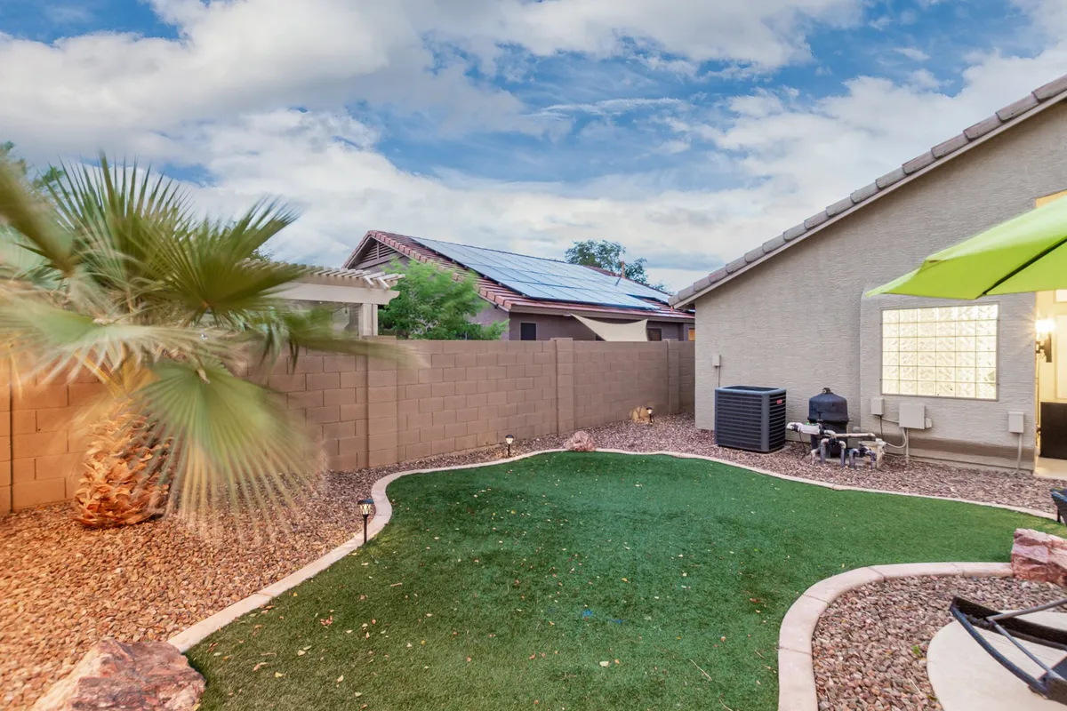 A lush artificial grass lawn framed by palm trees and a patio area with an umbrella. The scene is tranquil, inviting, and provides ample space for pets or yard games, while also offering peaceful spots for sunset watching or outdoor dining.