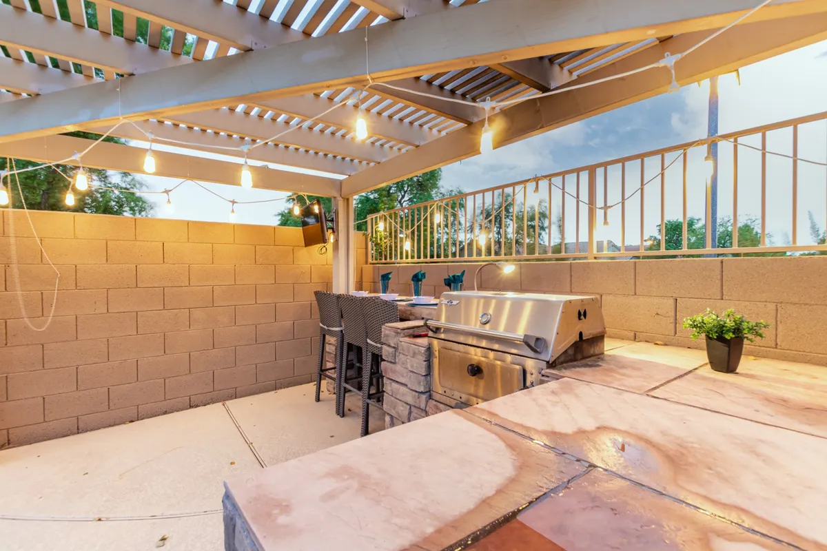 This outdoor scene showcases a grilling area with bar stools and string lights, creating an inviting atmosphere for socializing and dining after sports events.
